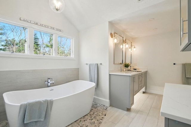 full bath with baseboards, a freestanding bath, lofted ceiling, and vanity