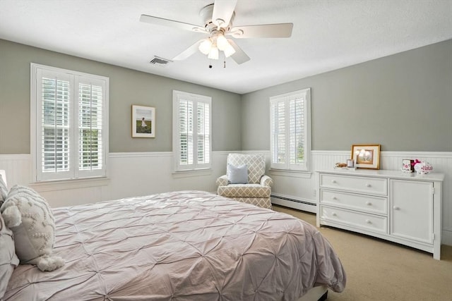 bedroom featuring ceiling fan, visible vents, carpet floors, a wainscoted wall, and a baseboard heating unit