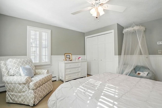 carpeted bedroom with a baseboard radiator, a wainscoted wall, ceiling fan, and a closet