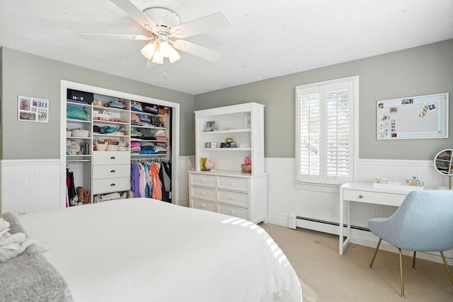 bedroom featuring light colored carpet, a ceiling fan, wainscoting, and a closet
