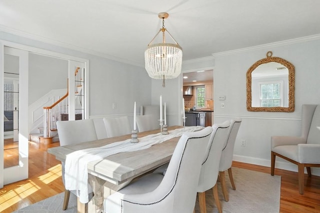 dining room featuring stairs, an inviting chandelier, ornamental molding, and light wood-type flooring
