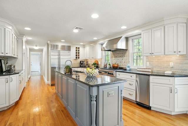 kitchen with wall chimney range hood, a sink, light wood finished floors, premium appliances, and white cabinetry