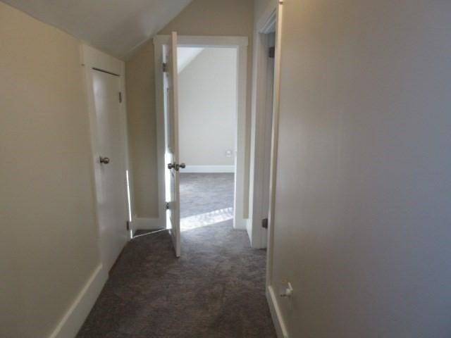 hallway featuring dark colored carpet, vaulted ceiling, and baseboards