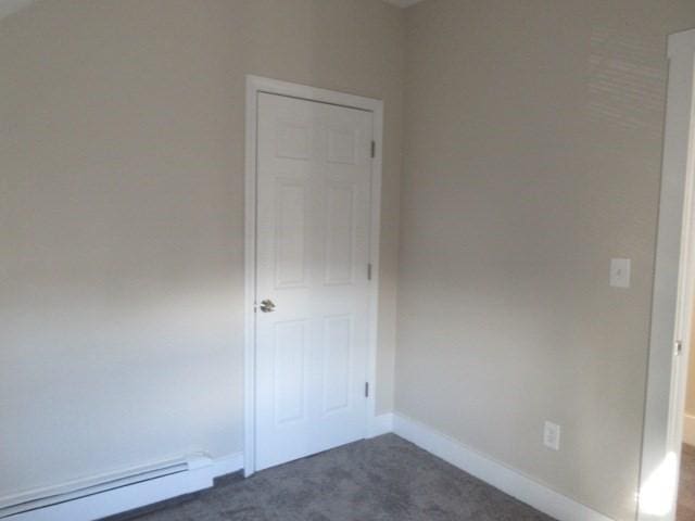 spare room featuring a baseboard radiator, dark carpet, and baseboards