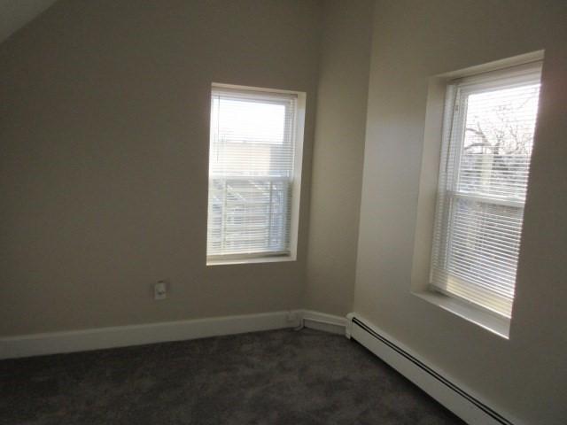 unfurnished room with baseboard heating, dark carpet, and baseboards