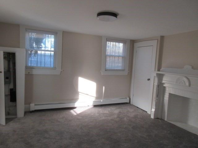unfurnished living room featuring carpet flooring, a fireplace, and a baseboard heating unit