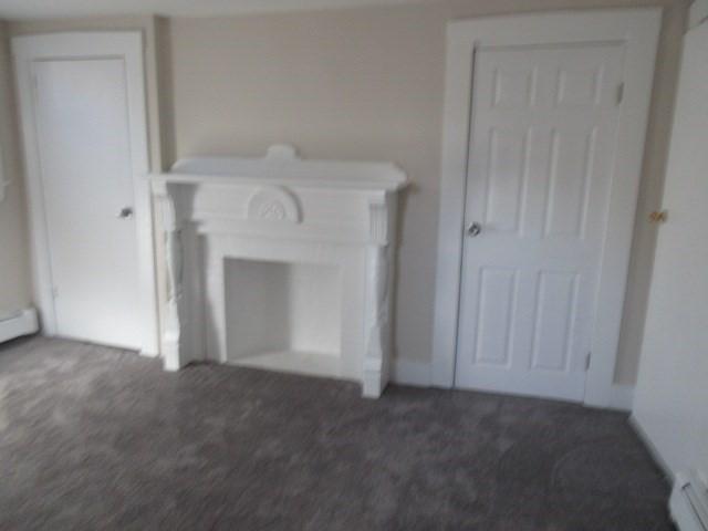 unfurnished living room featuring carpet and a baseboard heating unit