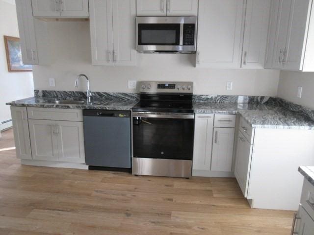 kitchen featuring appliances with stainless steel finishes, a sink, light wood-type flooring, and stone counters