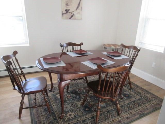 dining room with healthy amount of natural light, light wood-style floors, baseboards, and a baseboard heating unit