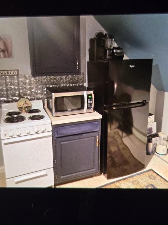 kitchen featuring black refrigerator, backsplash, dark brown cabinets, and white range with electric stovetop