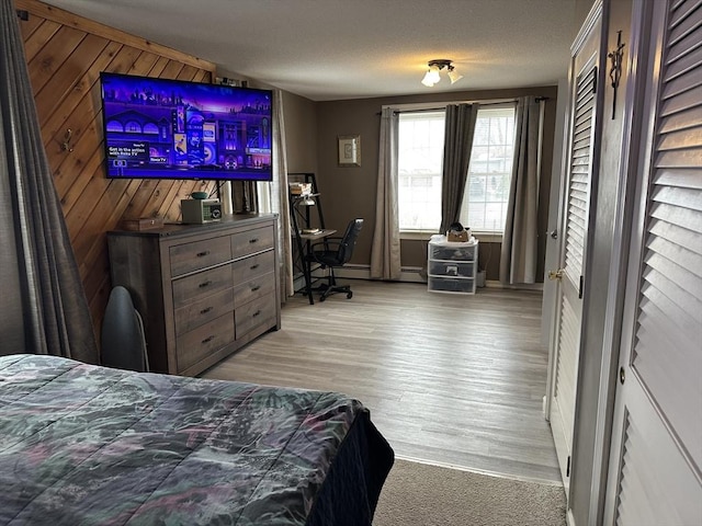 bedroom featuring a baseboard heating unit, light wood-type flooring, a textured ceiling, and wood walls