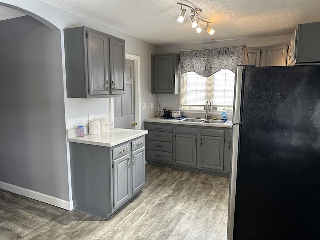 kitchen with sink, stainless steel refrigerator, gray cabinetry, hardwood / wood-style floors, and a textured ceiling