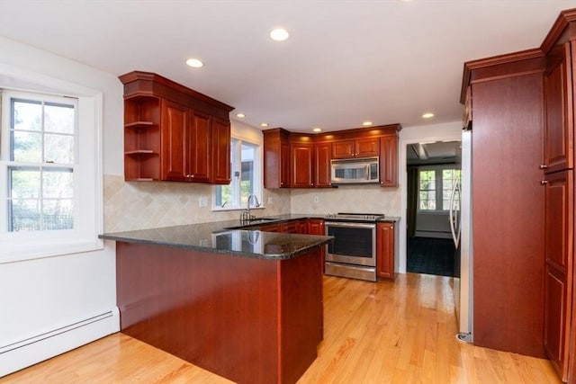 kitchen featuring a peninsula, light wood-style floors, a baseboard heating unit, tasteful backsplash, and appliances with stainless steel finishes