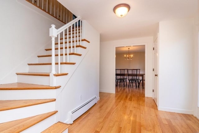 stairs featuring baseboards, a notable chandelier, a baseboard heating unit, and wood finished floors