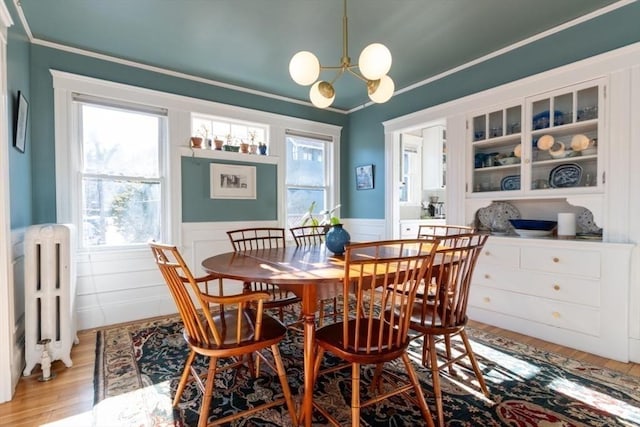 dining room with light wood finished floors, a wainscoted wall, radiator heating unit, ornamental molding, and an inviting chandelier