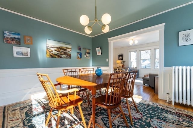 dining space featuring a notable chandelier, radiator, ornamental molding, wainscoting, and wood finished floors