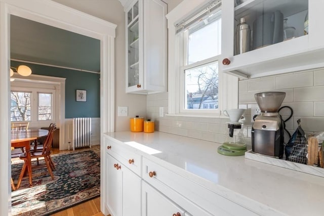 kitchen with white cabinets, light countertops, decorative backsplash, radiator heating unit, and glass insert cabinets