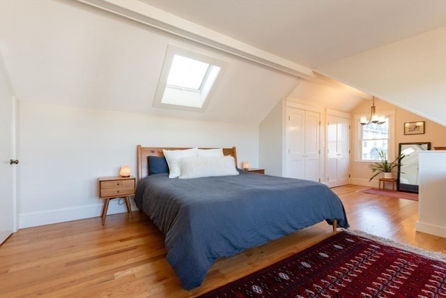 bedroom with baseboards, lofted ceiling with skylight, a chandelier, and light wood-style floors