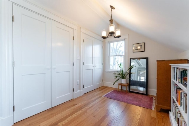 interior space with lofted ceiling, baseboards, a notable chandelier, and light wood-style floors