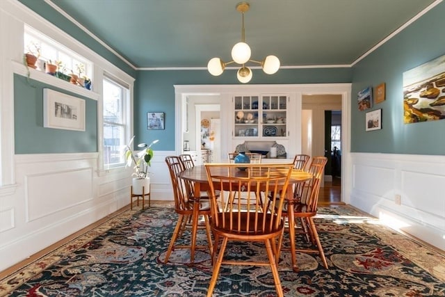 dining area with a chandelier, crown molding, and wainscoting