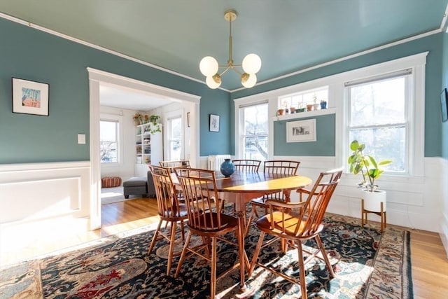 dining space featuring a wainscoted wall, a notable chandelier, ornamental molding, and wood finished floors