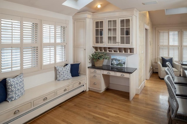 interior space featuring vaulted ceiling with skylight, baseboard heating, and light wood-style flooring