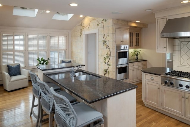 kitchen featuring a breakfast bar, a sink, light wood-style floors, appliances with stainless steel finishes, and wall chimney exhaust hood