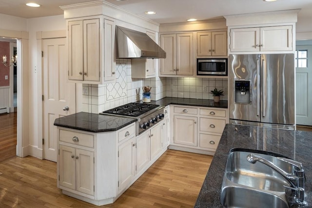 kitchen featuring light wood finished floors, appliances with stainless steel finishes, wall chimney exhaust hood, and a sink