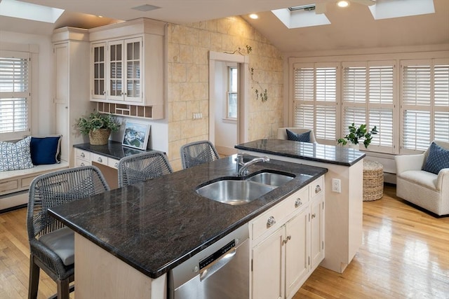 kitchen with a sink, light wood-type flooring, lofted ceiling with skylight, and stainless steel dishwasher