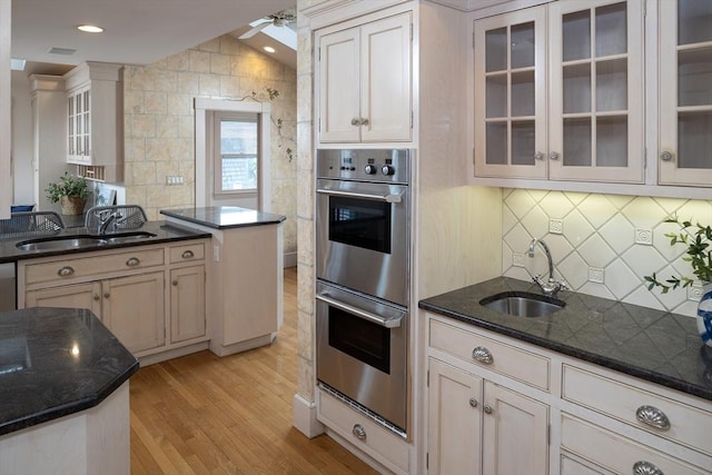 kitchen featuring tasteful backsplash, double oven, light wood-type flooring, and a sink