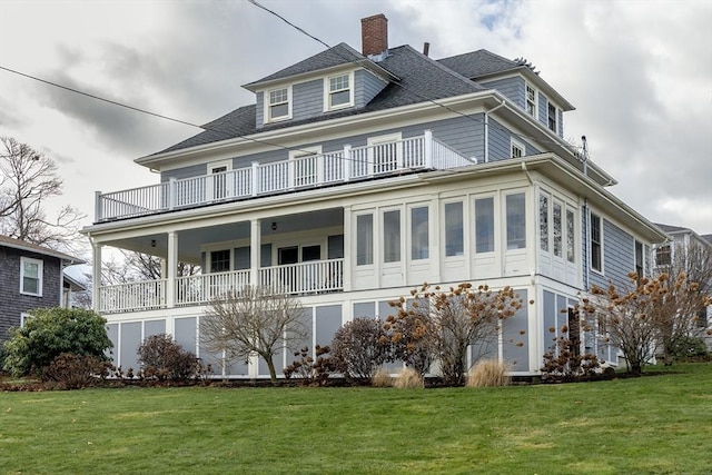 back of property featuring a yard, a balcony, and roof with shingles