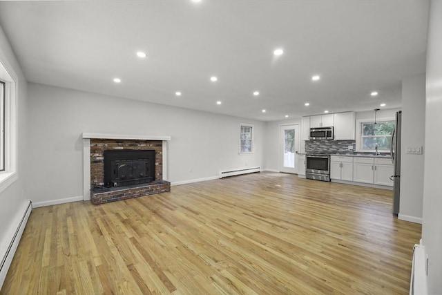 unfurnished living room featuring light hardwood / wood-style flooring, baseboard heating, and a brick fireplace