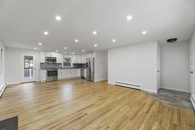 unfurnished living room with sink, baseboard heating, and light hardwood / wood-style flooring