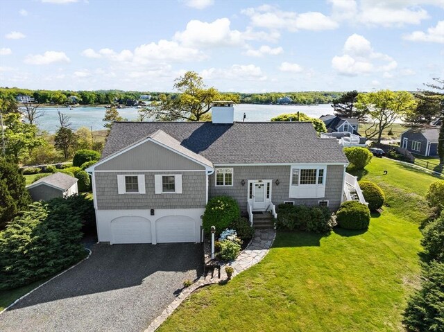 shingle-style home featuring a garage, a front lawn, a shingled roof, a water view, and a chimney