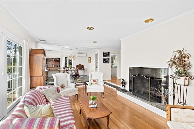 living area with light wood-style flooring, crown molding, a premium fireplace, a wall mounted air conditioner, and a chandelier