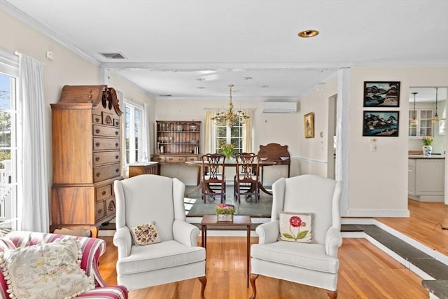 sitting room with a wall mounted AC, wood finished floors, ornamental molding, a chandelier, and baseboards