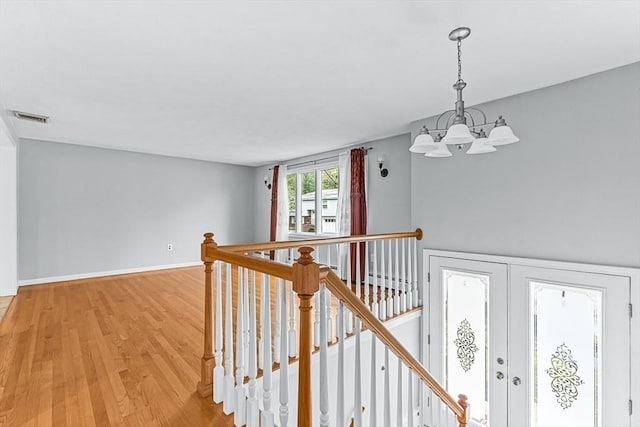 hall with an upstairs landing, a chandelier, light wood-type flooring, and baseboards