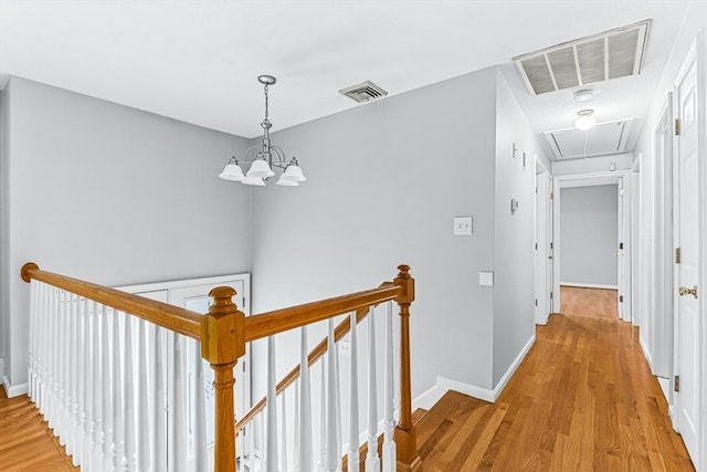 hallway with attic access, an upstairs landing, light wood finished floors, and a chandelier
