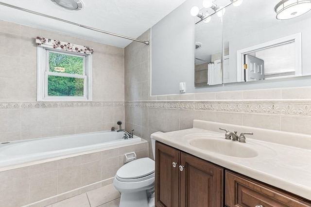 bathroom with tile walls, tiled tub, tile patterned flooring, toilet, and vanity