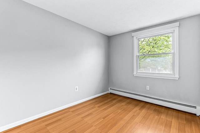 spare room with a baseboard radiator, light wood-type flooring, and baseboards