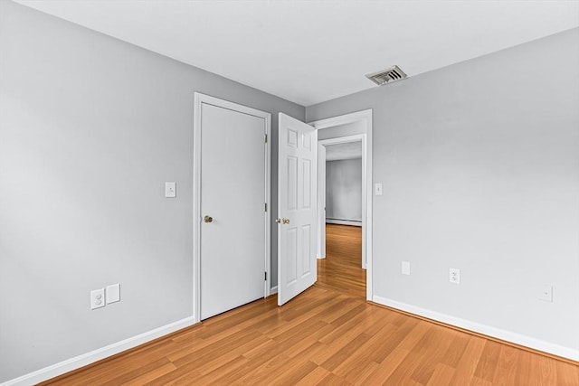 unfurnished bedroom with light wood-type flooring, baseboards, and baseboard heating