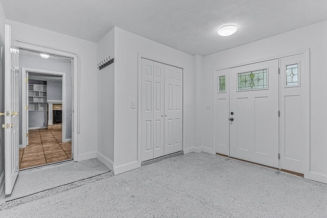 foyer entrance featuring baseboards, a textured ceiling, speckled floor, and a fireplace with raised hearth
