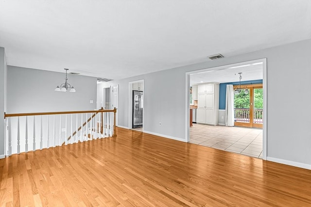 empty room featuring a chandelier, light wood-type flooring, and baseboards
