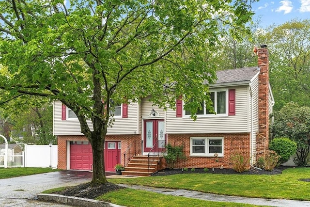 split foyer home featuring an attached garage, a chimney, asphalt driveway, and brick siding