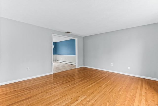 unfurnished room with a baseboard heating unit, light wood finished floors, and baseboards