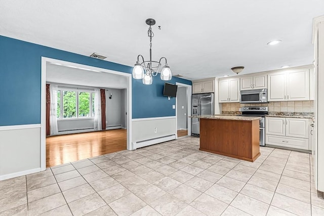 kitchen with appliances with stainless steel finishes, baseboard heating, light tile patterned floors, a kitchen island, and a chandelier