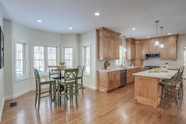 kitchen with sink, decorative light fixtures, a center island, light hardwood / wood-style flooring, and appliances with stainless steel finishes