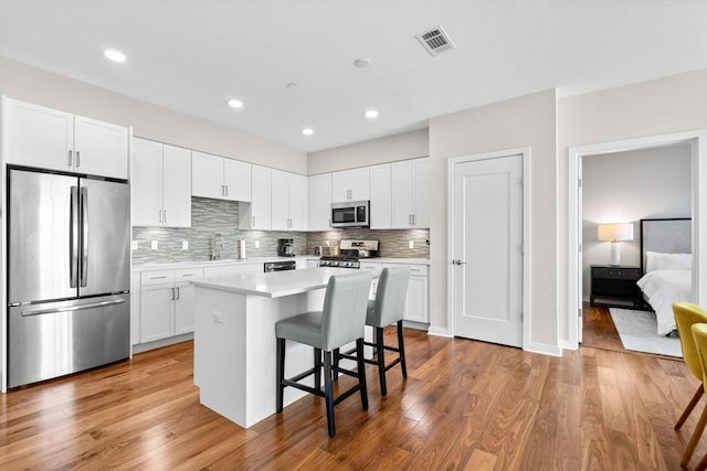 kitchen with appliances with stainless steel finishes, white cabinets, a kitchen island, light hardwood / wood-style flooring, and a breakfast bar