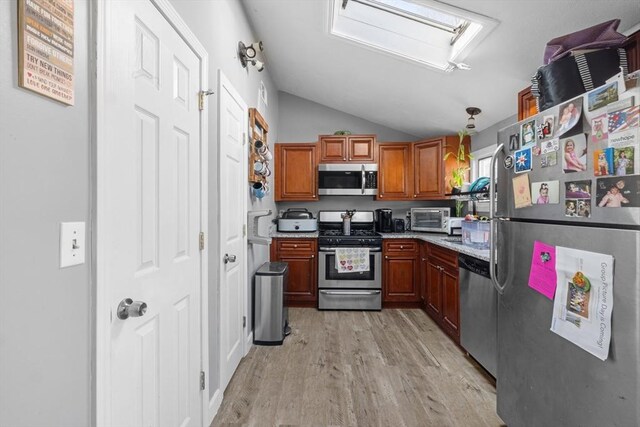 kitchen featuring light wood-style flooring, stainless steel appliances, brown cabinetry, a toaster, and vaulted ceiling