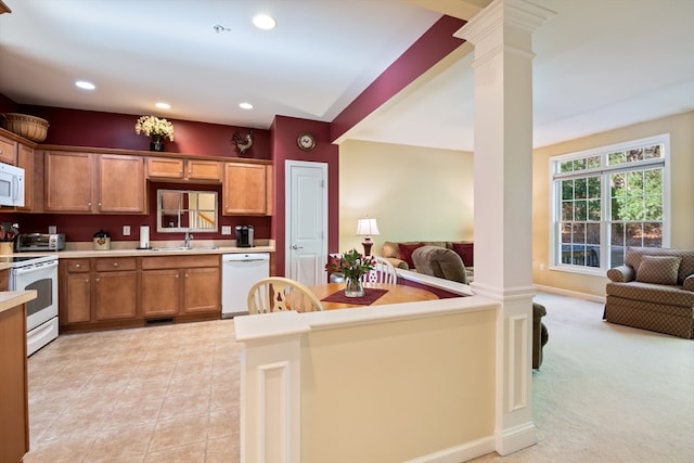 kitchen with light colored carpet, white appliances, sink, and ornate columns